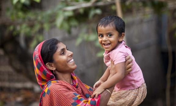 Photo of a woman holding an infant in the air. Source: Drik/USAID