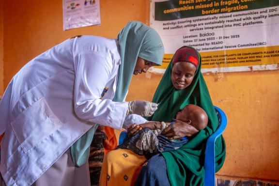 A woman immunizing an infant held by its mother